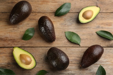 Whole and cut avocados with green leaves on wooden table, flat lay