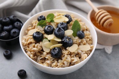 Photo of Tasty oatmeal with blueberries, mint and almond petals in bowl on grey table