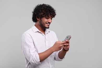Handsome smiling man using smartphone on light grey background, space for text