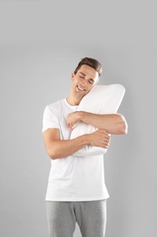 Photo of Young man in pajamas embracing pillow on gray background