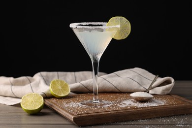Photo of Martini glass of refreshing cocktail with lime and sugar on wooden table against black background
