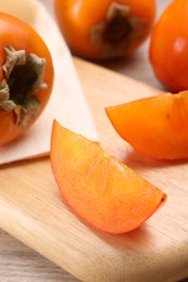 Photo of Delicious ripe persimmons on wooden board, closeup