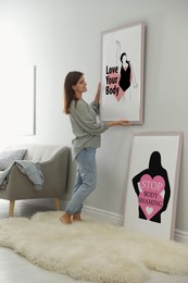 Image of Stop body shaming and love yourself. Smiling woman hanging body positive posters on wall in room