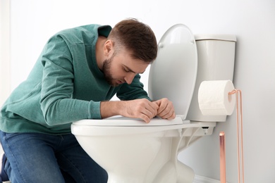 Young man suffering from nausea over toilet bowl indoors