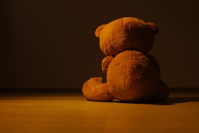 Cute lonely teddy bear on floor in dark room, back view. Space for text