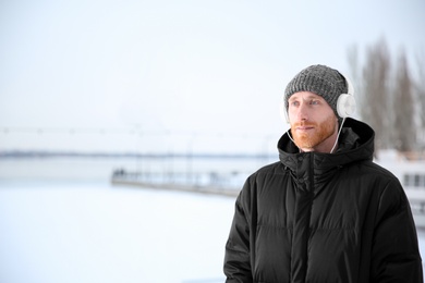 Photo of Young man listening to music with headphones outdoors. Space for text