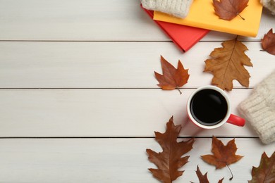 Cup of hot coffee, books, sweater and autumn leaves on white wooden table, flat lay. Space for text