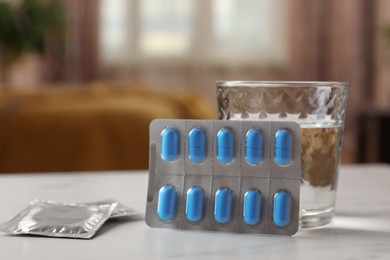 Photo of Glass of water, condoms and pills on white table indoors, closeup with space for text. Potency problem concept