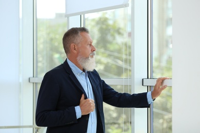 Portrait of handsome mature man in elegant suit looking out window indoors