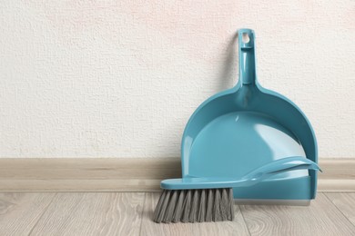 Photo of Plastic whisk broom with dustpan near light wall indoors. Space for text