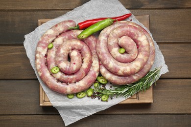 Photo of Board with homemade sausages, rosemary, chili and spices on wooden table, top view