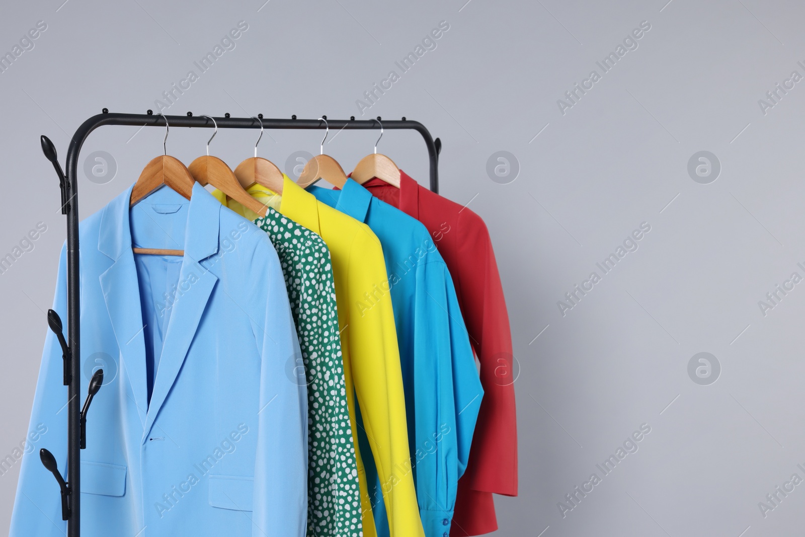 Photo of Rack with stylish women`s clothes on wooden hangers against light grey background, space for text