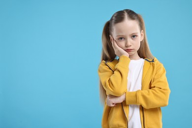 Portrait of sad girl on light blue background, space for text