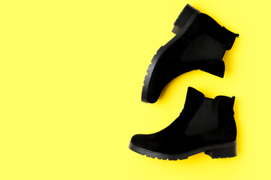 Photo of Stylish black female boots on yellow background, flat lay. Space for text