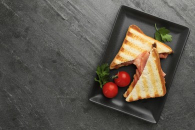Photo of Tasty sandwiches with ham, parsley, tomatoes and cheese on dark grey textured table, flat lay. Space for text