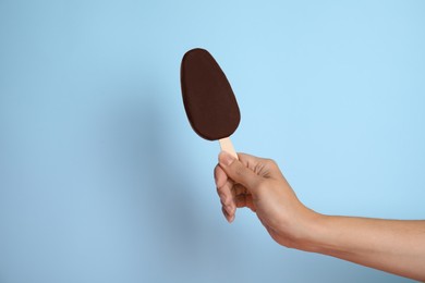 Photo of Woman holding ice cream glazed in chocolate on light blue background, closeup
