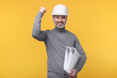 Photo of Architect in hard hat holding folders on orange background