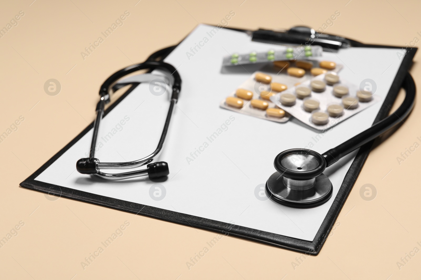 Photo of Stethoscope, pills and clipboard on beige background, closeup. Medical tool