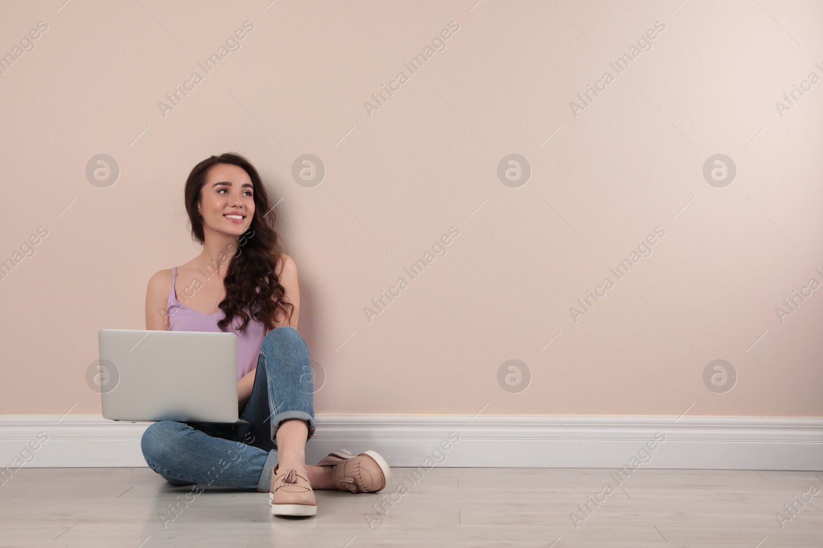 Photo of Young woman sitting with laptop near beige wall. Space for text