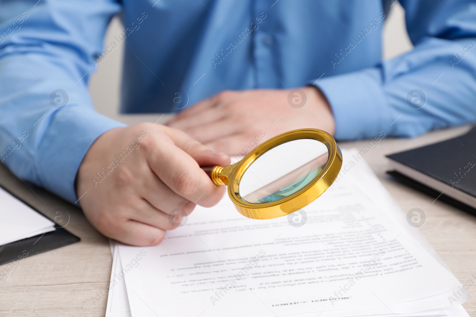 Photo of Man looking at document through magnifier at white wooden table, closeup. Searching concept