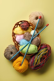 Photo of Soft woolen yarns and knitting needles on yellow background, flat lay