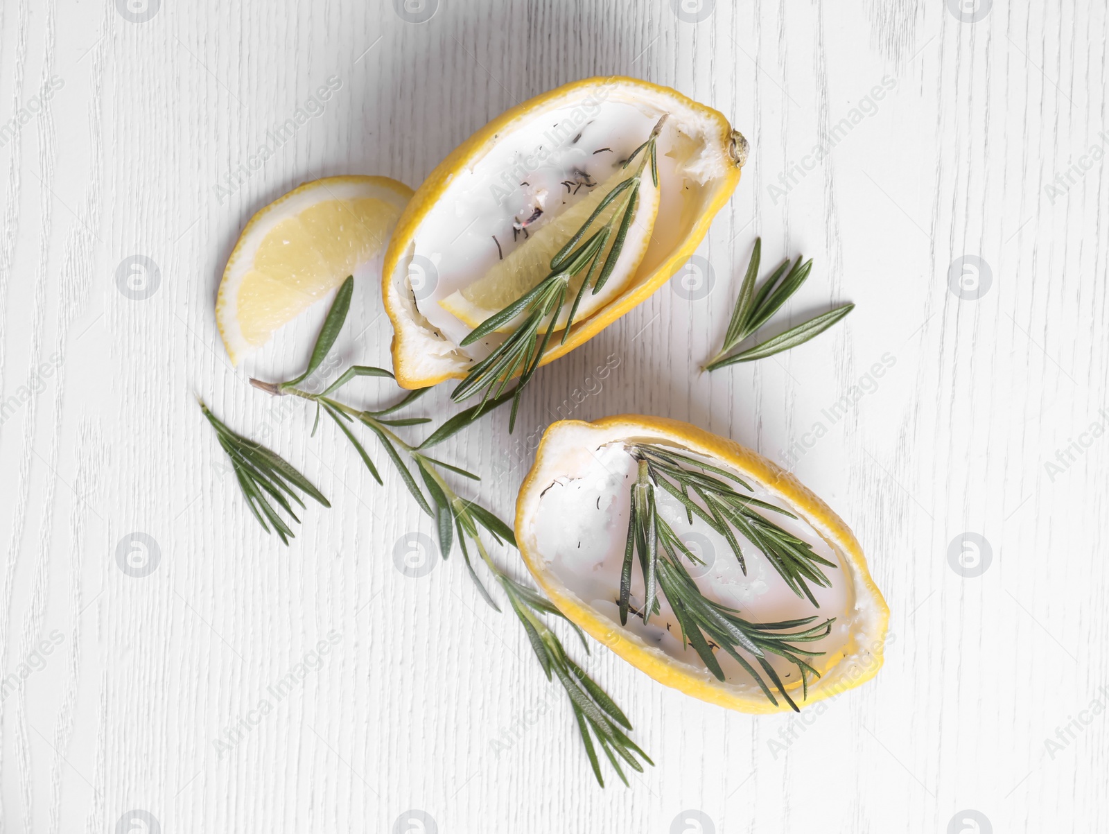 Photo of Lemon candles and fresh rosemary on white wooden table, flat lay. Natural homemade repellent