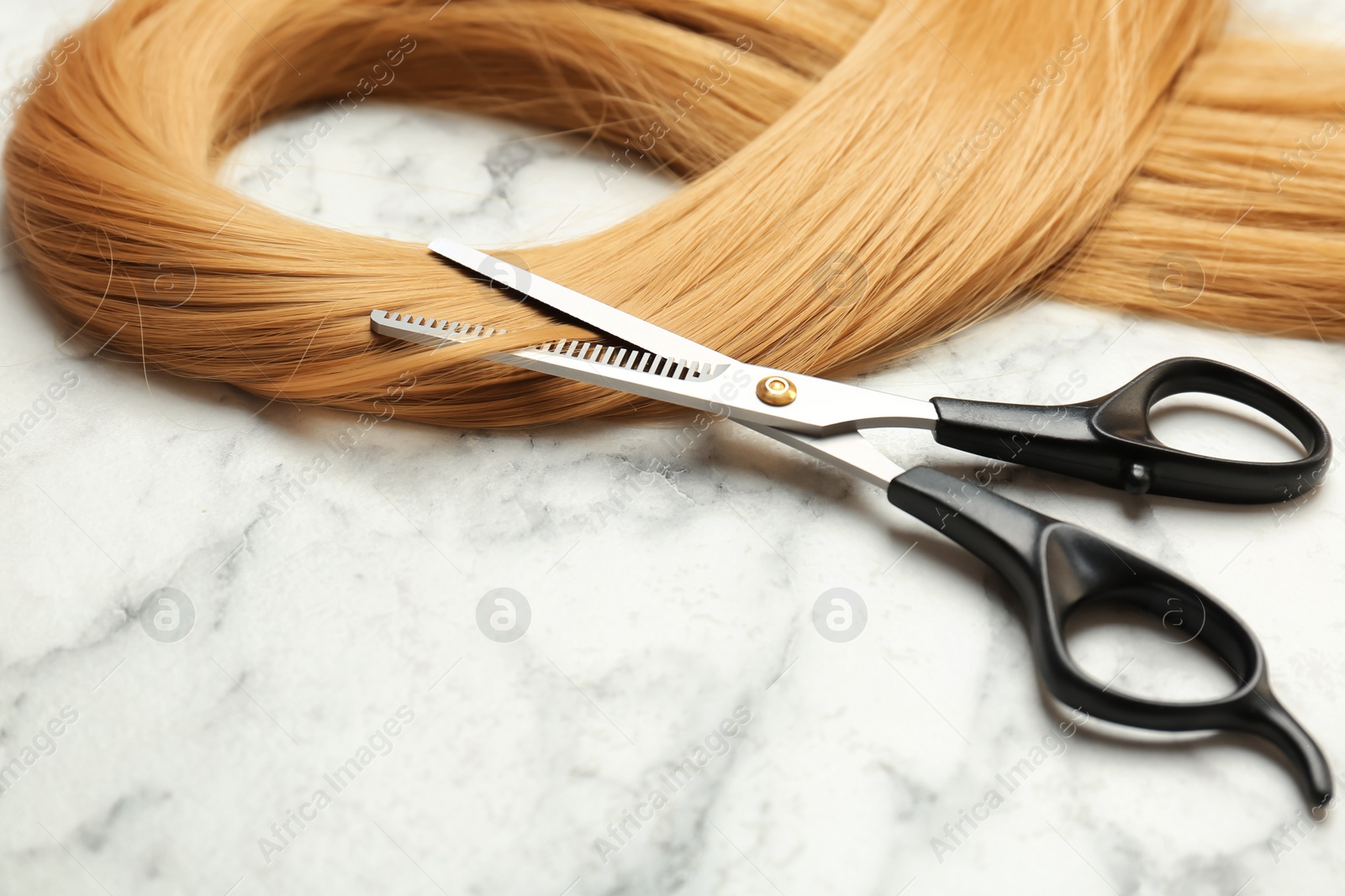 Photo of Professional hairdresser scissors and strand of blonde hair on marble background