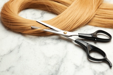 Photo of Professional hairdresser scissors and strand of blonde hair on marble background