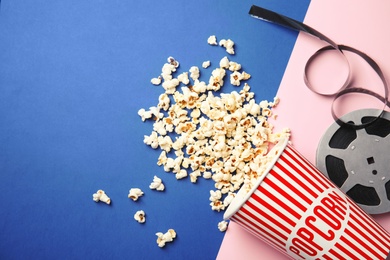 Tasty popcorn and film reel on color background, top view with space for text. Cinema snack