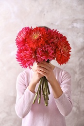 Photo of Woman hiding behind beautiful dahlia flowers on color background