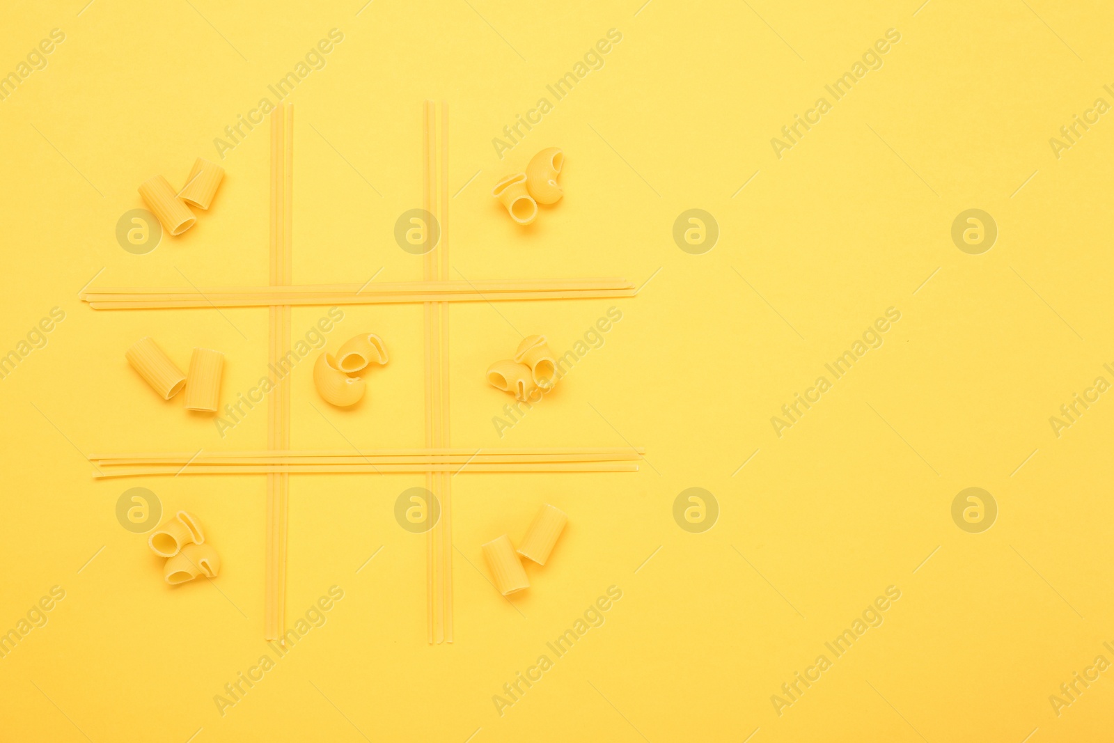 Photo of Tic tac toe game made with different types of pasta on yellow background, top view