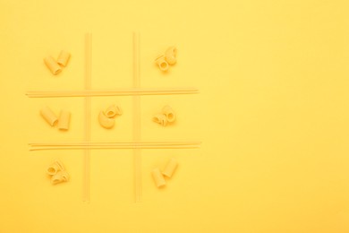 Photo of Tic tac toe game made with different types of pasta on yellow background, top view