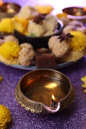 Photo of Diwali celebration. Diya lamp on shiny violet table, closeup