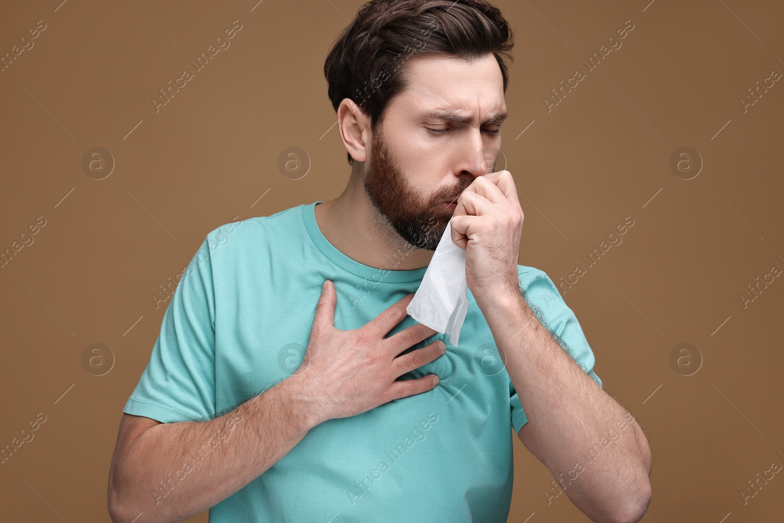 Photo of Sick man with tissue coughing on brown background