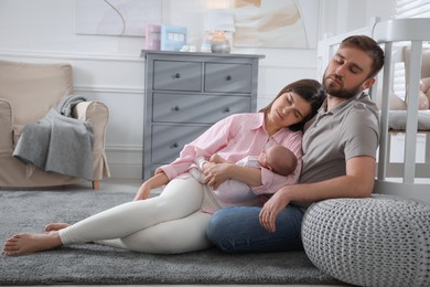 Tired young parents with their baby sleeping on floor in children's room
