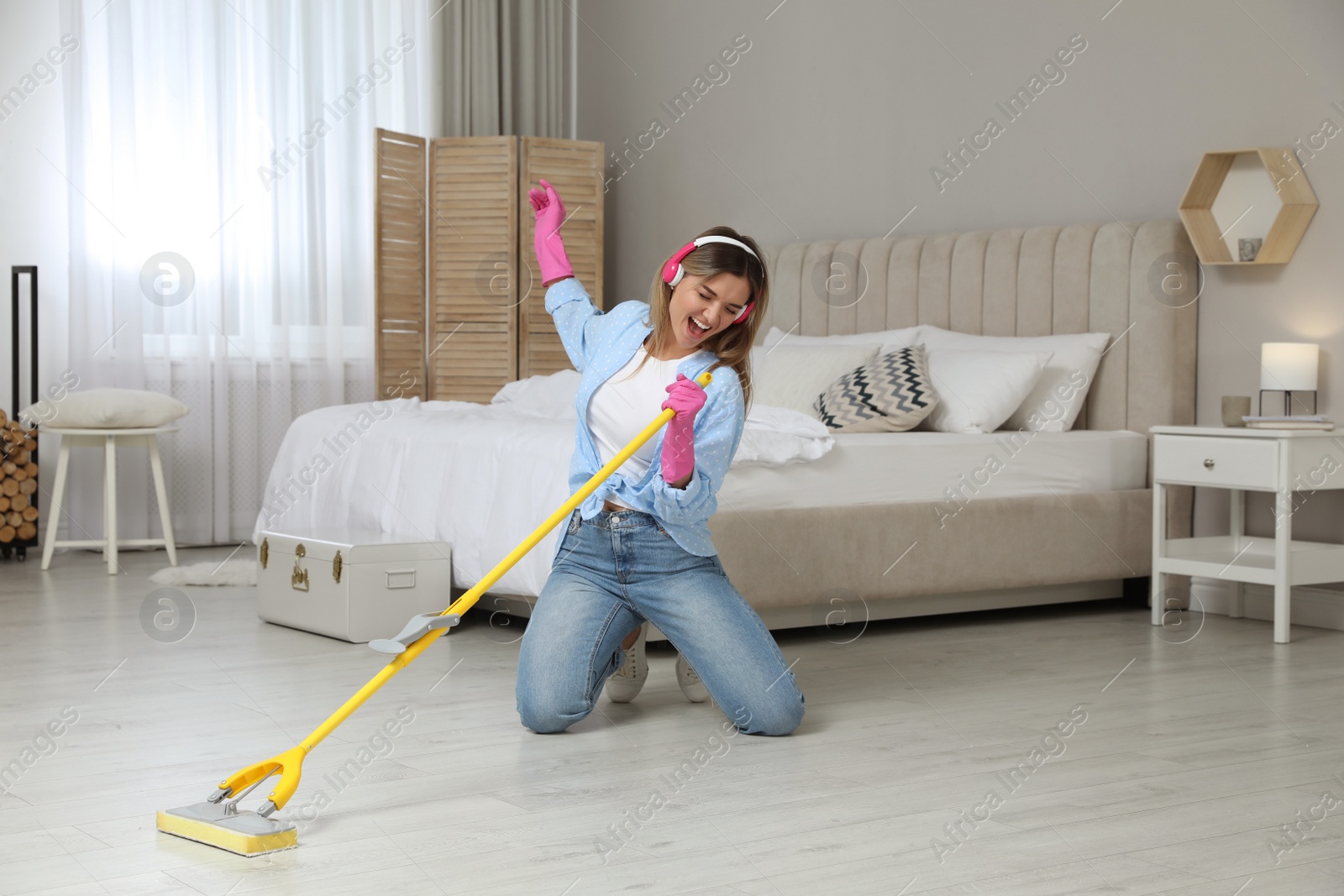 Photo of Woman in headphones with mop singing while cleaning at home