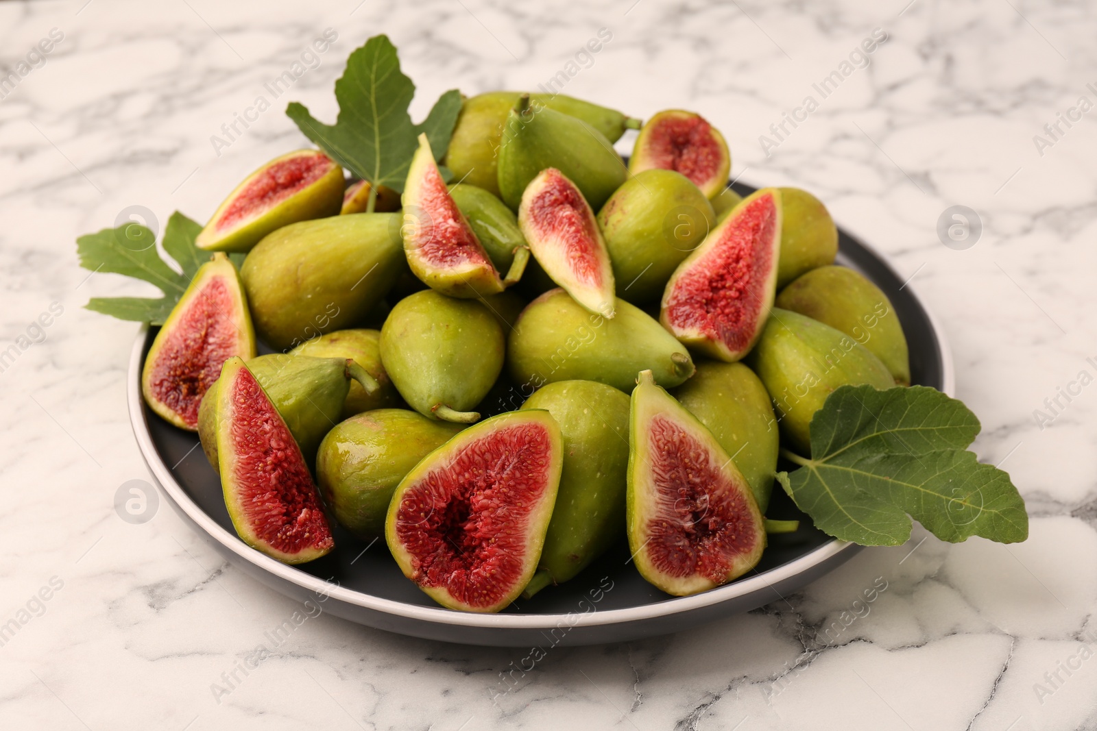 Photo of Cut and whole green figs on white marble table, closeup