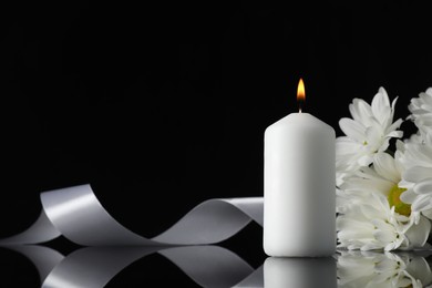 Photo of Burning candle, white chrysanthemum flowers and ribbon on black mirror surface in darkness, closeup with space for text. Funeral symbols