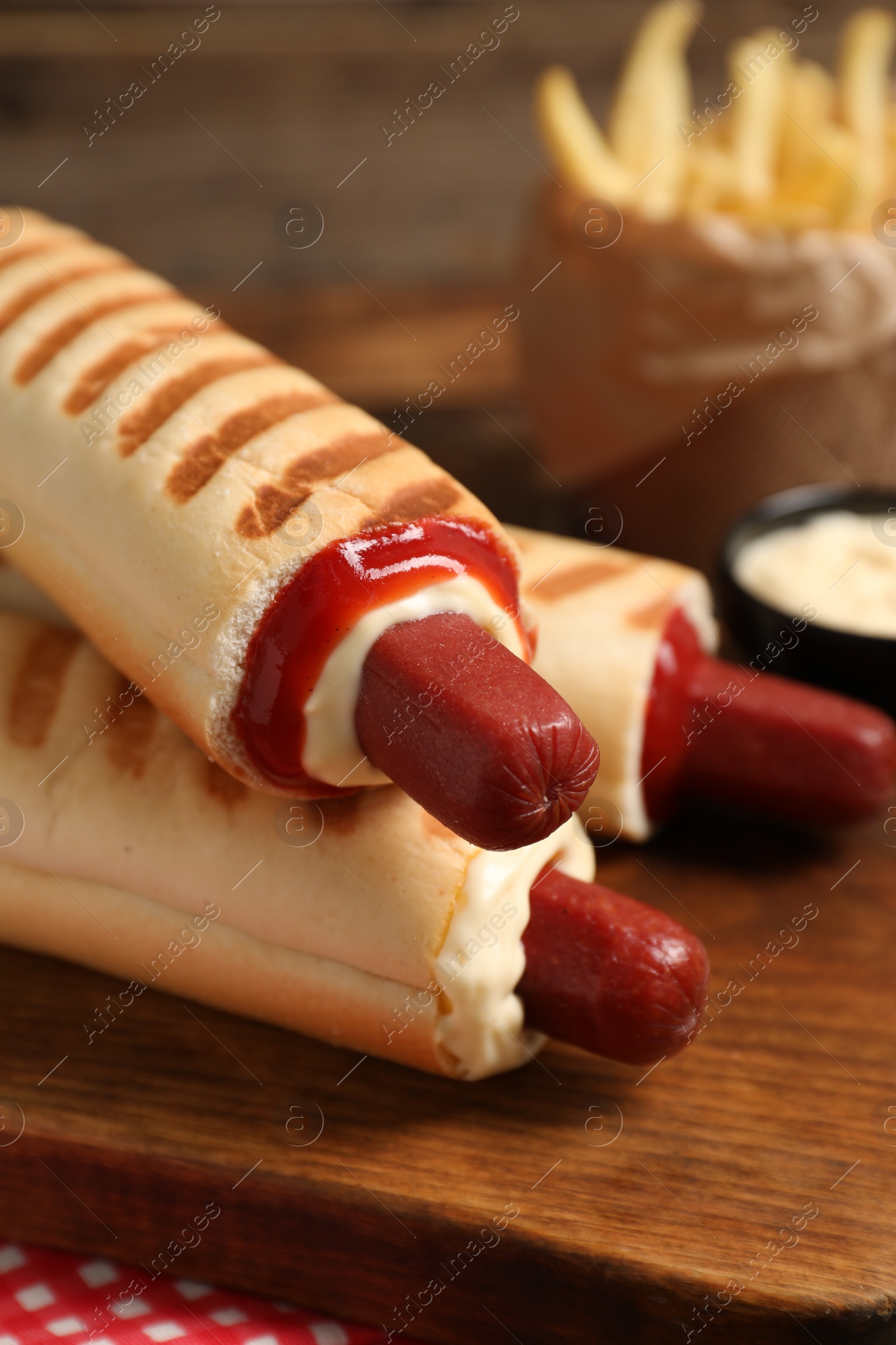 Photo of Delicious french hot dogs, fries and dip sauce on wooden board, closeup