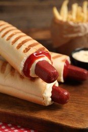 Delicious french hot dogs, fries and dip sauce on wooden board, closeup