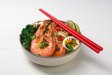 Delicious ramen with shrimps, egg and chopsticks on white wooden table. Noodle soup