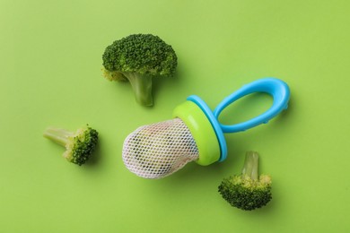 Nibbler with boiled broccoli on green background, flat lay. Baby feeder