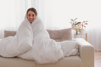 Woman wrapped in blanket resting on sofa, space for text