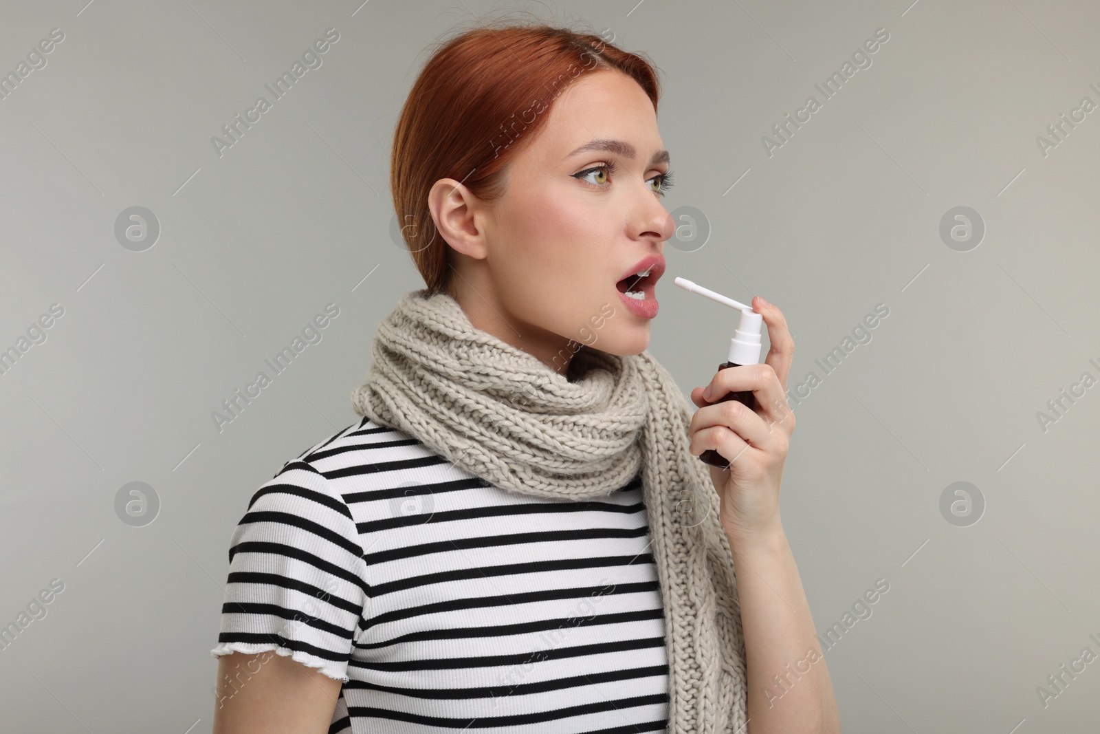 Photo of Young woman with scarf using throat spray on grey background