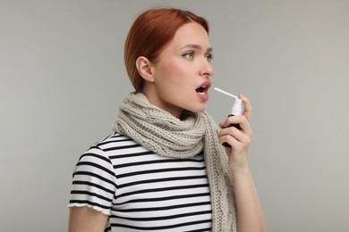 Young woman with scarf using throat spray on grey background