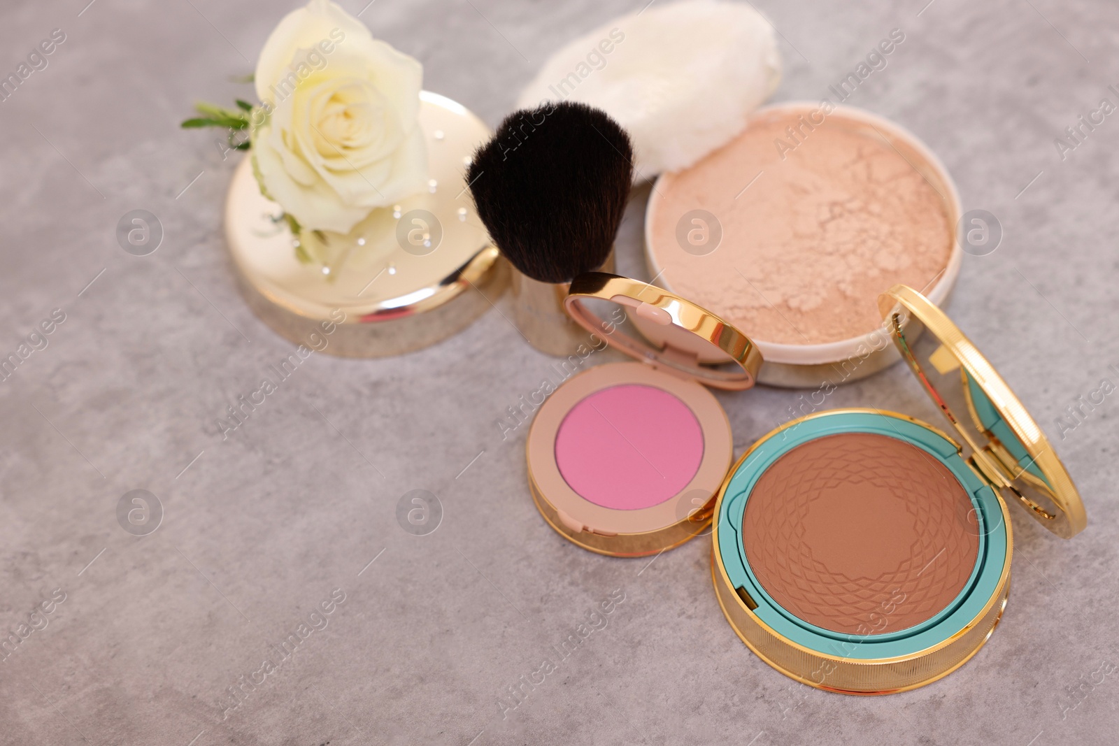 Photo of Bronzer, powder, blusher, brush and rose flower on grey textured table, above view