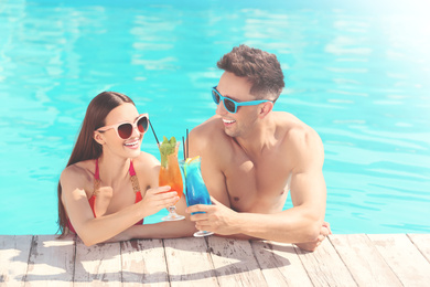 Image of Happy young couple with cocktails in swimming pool