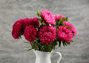 Beautiful pink asters in jug on grey background. Autumn flowers