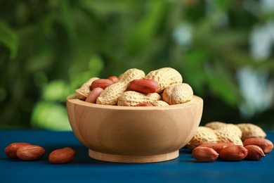 Photo of Fresh unpeeled peanuts in bowl on blue wooden table against blurred background