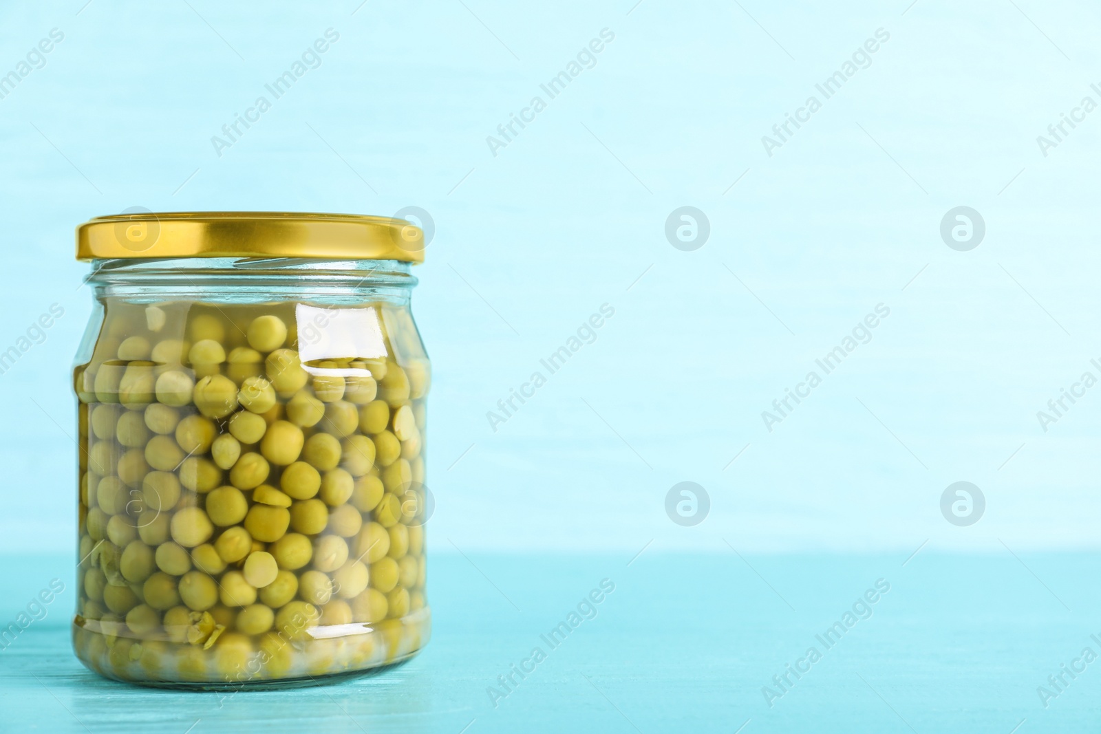 Photo of Glass jar of pickled green peas on light blue wooden table. Space for text